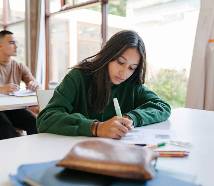 A student sitting in a classroom highlighting notes